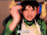 a man wearing headphones and a green shirt is making a funny face and saying huh ?