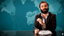a man in a suit and tie is sitting at a desk in front of a map of the world