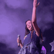 a woman is singing into a microphone with her arms in the air