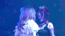 a couple of women are standing next to each other on a stage in front of a blue light .