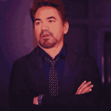 a man with a beard wearing a suit and tie with his hands folded