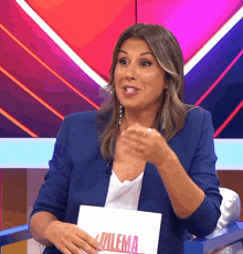 a woman in a blue jacket is sitting in front of a sign that says dilema