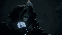 a monster with a hood on holds a glowing crystal