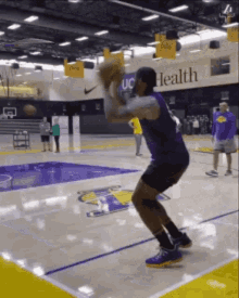 a man in a purple shirt is playing basketball on a court with a sign that says health on it