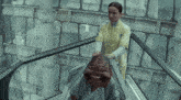 a woman in a yellow coat is standing next to a man with a huge head