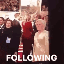 a woman in a gold dress is standing on a red carpet in front of a crowd of people .