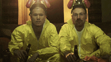 two men in yellow suits are sitting on a couch holding beer