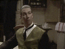 a man wearing a yellow and black striped vest and tie is sitting at a table