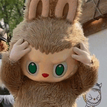 a stuffed animal with green eyes holds its hands on its head