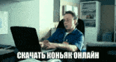a man in a blue shirt is typing on a laptop with the words " скачать коньяк онлайн " above him