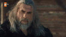 a man with long hair and a beard is standing in front of a wall .