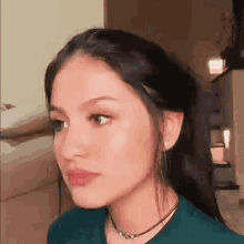 a close up of a woman 's face wearing a green shirt and a choker .
