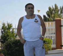 a man wearing a white tank top with a monkey on it stands in front of a fence