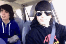 a man wearing sunglasses and a bandana is driving a car with another man sitting in the back seat .