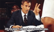 a man in a suit and tie is sitting at a desk saying oh my god i do not have time for you .