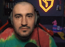 a man with a beard wearing headphones and a tie dye shirt looks at the camera