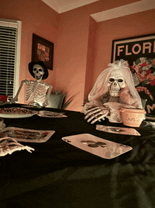a skeleton in a bride costume sits at a table with cards and a bowl that says sun on it