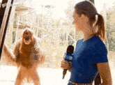 a woman in a blue shirt is holding a microphone in front of an orangutan