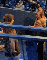 a group of people are sitting in a stadium behind a blue railing