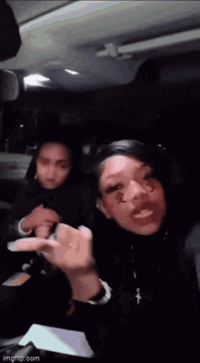 two women are sitting in the back seat of a car and one has a cross on her neck .