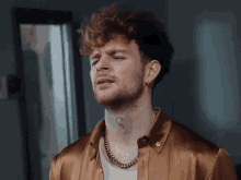 a man with curly hair and a tattoo on his neck has a gold chain around his neck .
