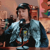 a man wearing headphones and a denim vest is holding a can of soda in front of a microphone