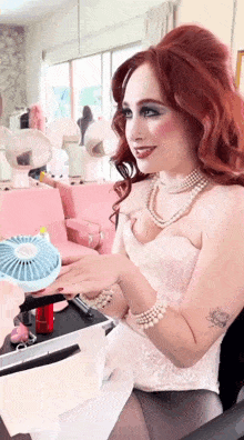 a woman in a white dress and pearls is holding a small fan