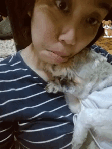a woman in a blue and white striped shirt is holding a small white dog