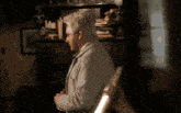 a man with white hair stands in front of a bookcase