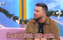 a man with a beard is sitting on a pink couch and says " e impossivel ser assim "