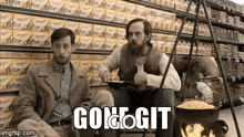two men are sitting next to each other in front of a pot of food in a store .