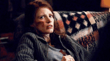 a woman in a sweater sits on a couch with a blanket on it