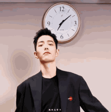 a man in a suit stands in front of a clock that shows the time as almost 5:00