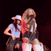 a woman in a cowboy hat is singing into a microphone while standing next to another woman .