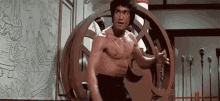 bruce lee is standing in front of a wooden wheel .