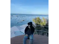 a person wearing a black hoodie with the word balenciaga on it sits on a deck overlooking the ocean