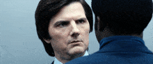 a man in a suit is looking at another man in a blue suit