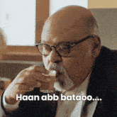 a man with glasses and a beard drinking from a glass with the words haan abb bataoo written on the bottom