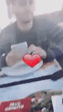 a man is sitting in a car looking at his phone with a red heart in front of him