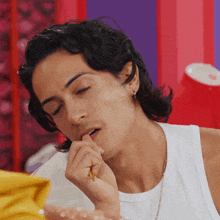 a man in a white tank top has his eyes closed and his hand in his mouth