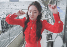 a woman in a red dress is standing in a stadium with her arms in the air