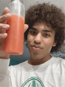 a young man with curly hair is holding a bottle of red liquid in his hand
