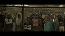 a group of people behind a chain link fence holding pictures of people