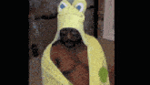a man is wrapped in a yellow towel with a frog hat on his head .