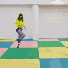 a woman in a yellow hoodie is dancing on a multicolored floor