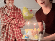 a man in a plaid shirt is holding a cake with candles and a balloon with the number 20 on it