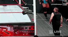 a man in a black vest is standing in a wrestling ring with a red rope .