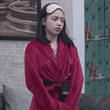 a woman in a red robe and headband is standing in front of a couch .