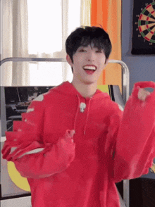 a young man in a red hoodie is standing in front of a dartboard .