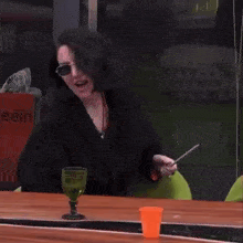 a woman is sitting at a table holding a stick and a glass .